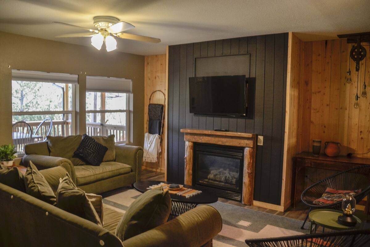 A cozy living room with a fireplace, a television mounted on the wall, and a ceiling fan.