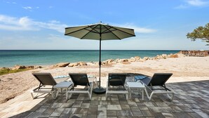 A beachside patio with four lounge chairs and a table under an umbrella, overlooking the ocean. - Beach Amore | Ocean front | Pool | 365 Sunsets a Year (Englewood)