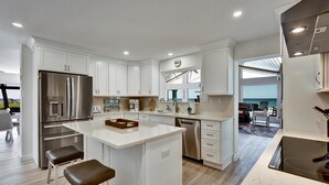 A modern kitchen with white cabinetry, a stainless steel refrigerator, and a central island with stools. - Beach Amore | Ocean front | Pool | 365 Sunsets a Year (Englewood)