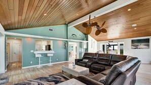 A spacious living area with a large leather sofa, a coffee table, and a marble ottoman. A ceiling fan and recessed lighting are visible. - Beach Amore | Ocean front | Pool | 365 Sunsets a Year (Englewood)