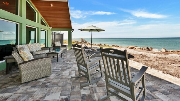 A patio area with outdoor furniture, a view of the ocean, and a covered seating area with large windows. - Beach Amore | Ocean front | Pool | 365 Sunsets a Year (Englewood)