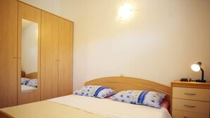 Een slaapkamer met een bed, nachtkastje met lamp, een dressoir en een kledingkast.