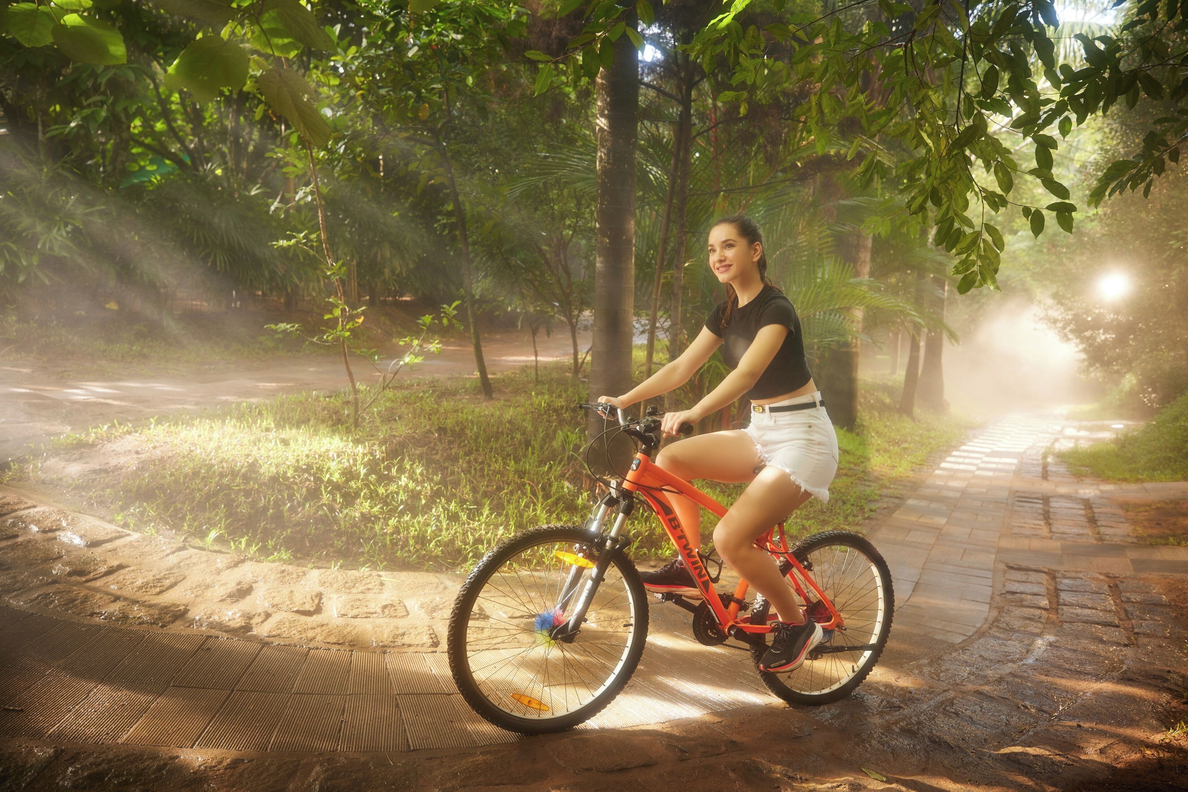 A person riding a mountain bike on a paved path surrounded by greenery.