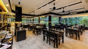 A spacious restaurant with multiple dining tables and chairs, a buffet area, and large windows offering a view of the outdoors. - Casa Rio Resort Athirapilly (Chalakudy)