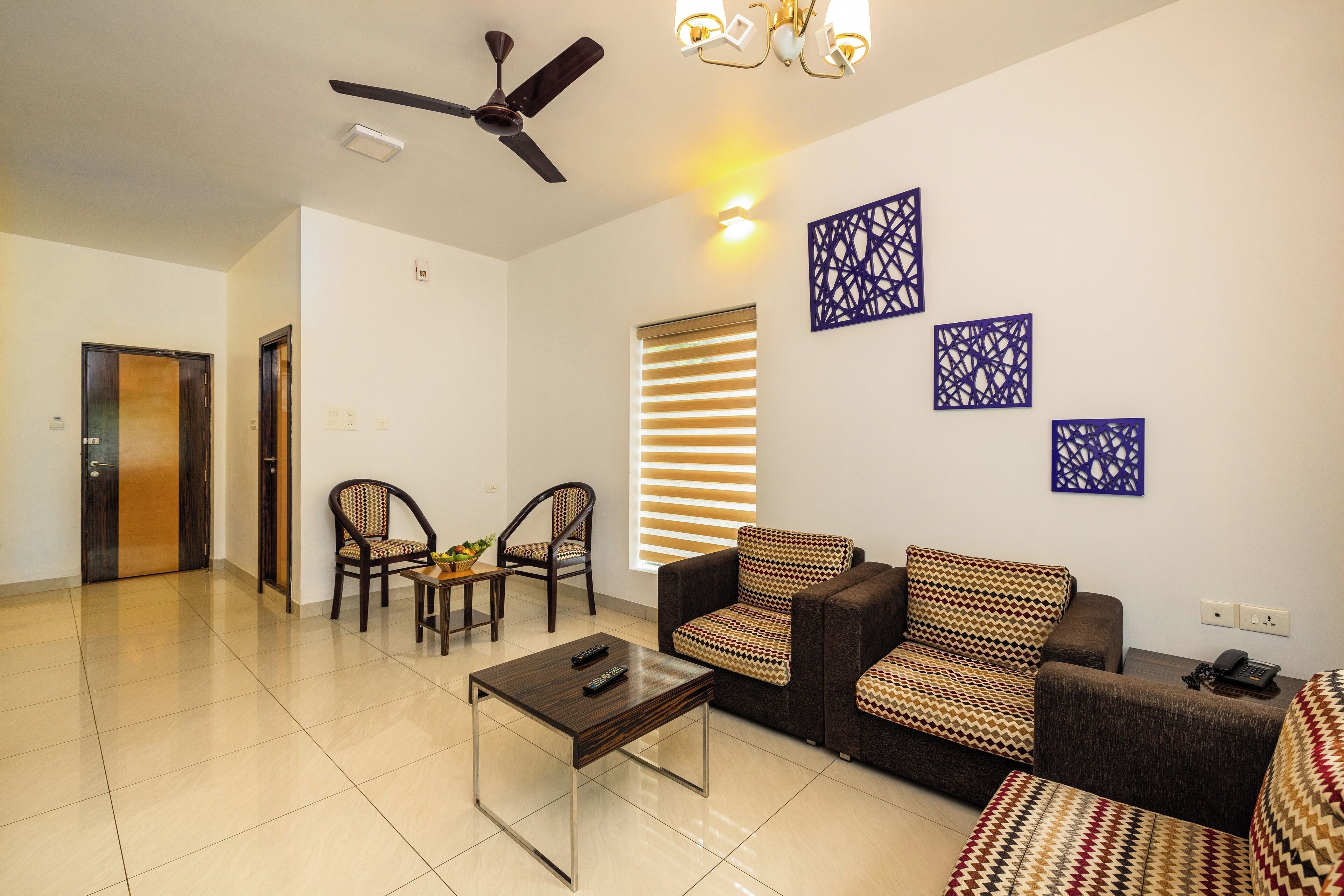 A spacious living room with a ceiling fan, a sofa set, two armchairs, a coffee table, and a TV.