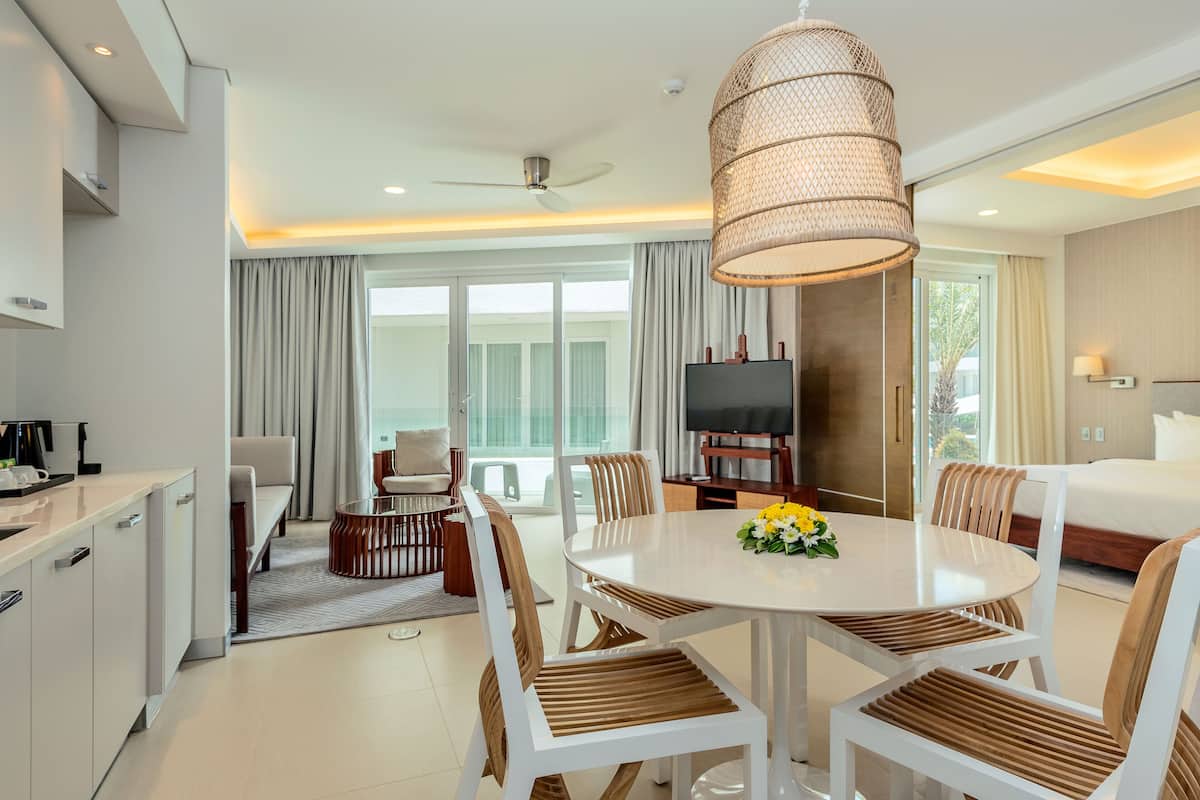 Una habitación de hotel moderna con comedor, televisor y balcón con cortinas.