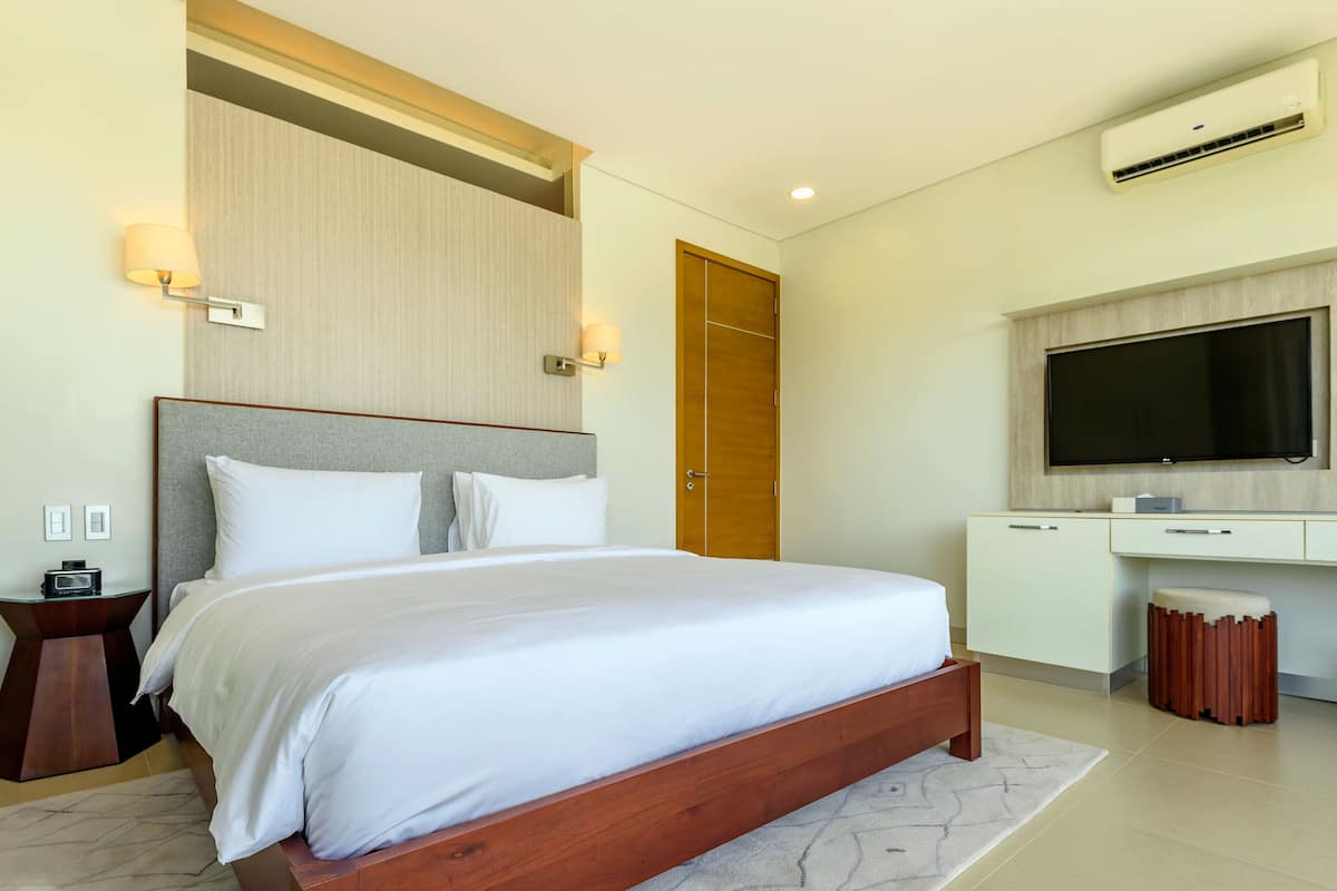 Una habitación de hotel moderna con una cama grande, un escritorio, un televisor y un aire acondicionado.