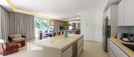 A modern kitchen with a central island, white cabinetry, and a dining area with a sofa and chairs.