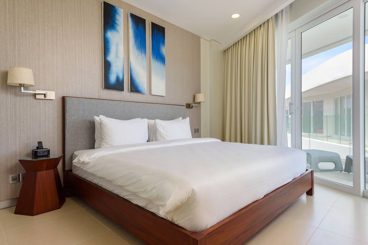 Habitación de hotel moderna con una cama grande, dos lámparas fijadas a la pared y un ventanal con cortinas.