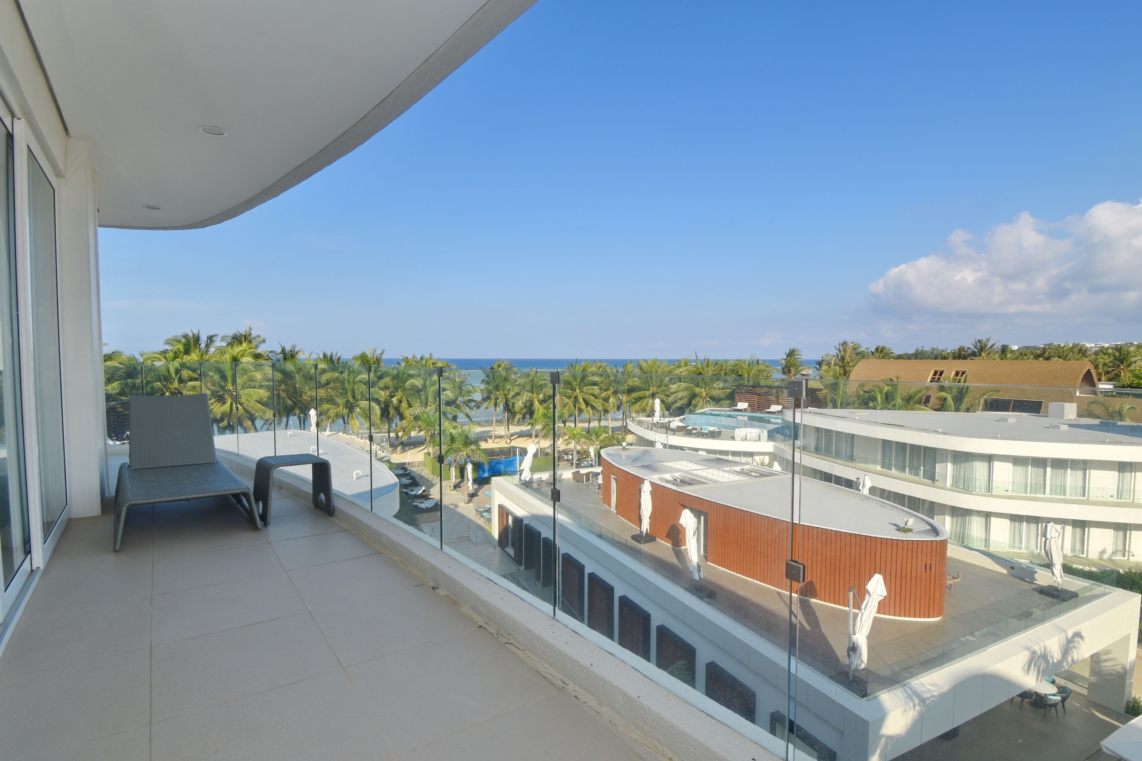 Un balcón con vista al océano, palmeras y una zona de piscina.