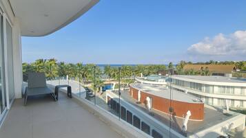 A balcony with a view of the ocean, palm trees, and a pool area.
