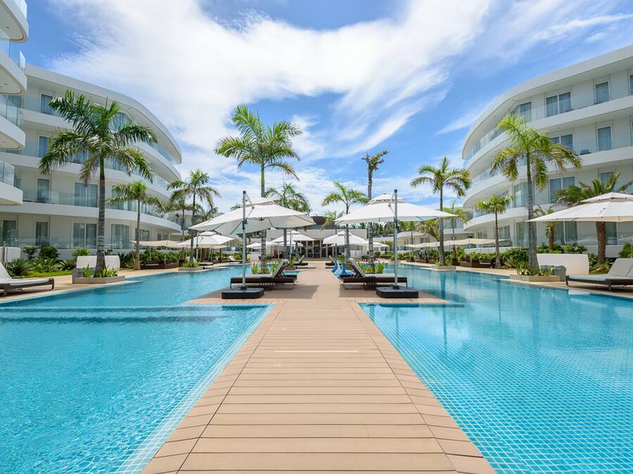 Un hotel moderno con una piscina central, varios balcones y palmeras.