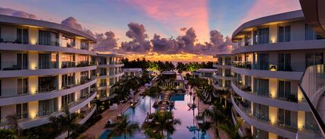 A multi-story hotel with a central pool, balconies, and palm trees.