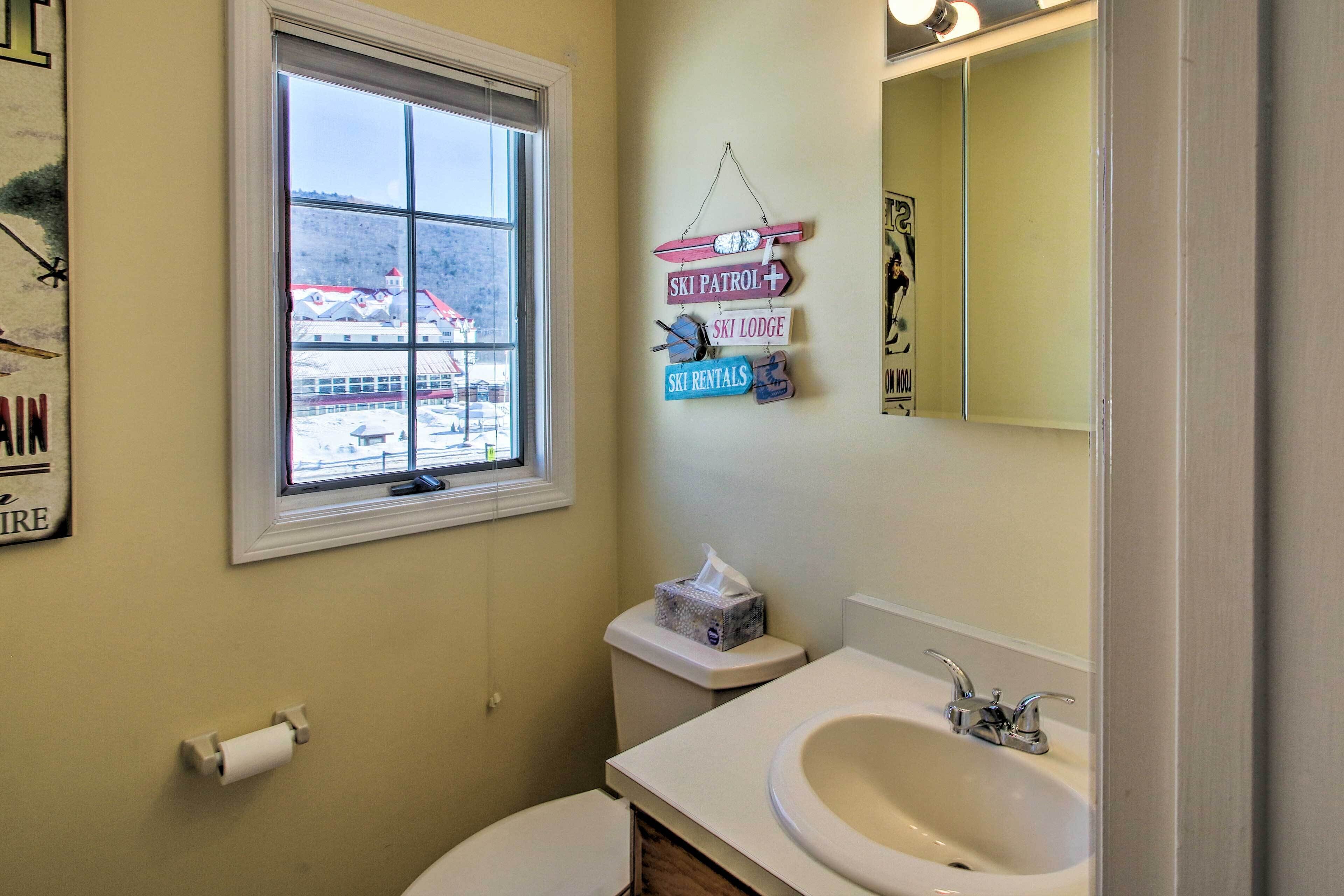 Une salle de bain avec des toilettes, un lavabo et une fenêtre. Des panneaux sont affichés sur le mur indiquant l’emplacement du service de sécurité des pistes, du refuge de ski et du point de location de matériel de ski.