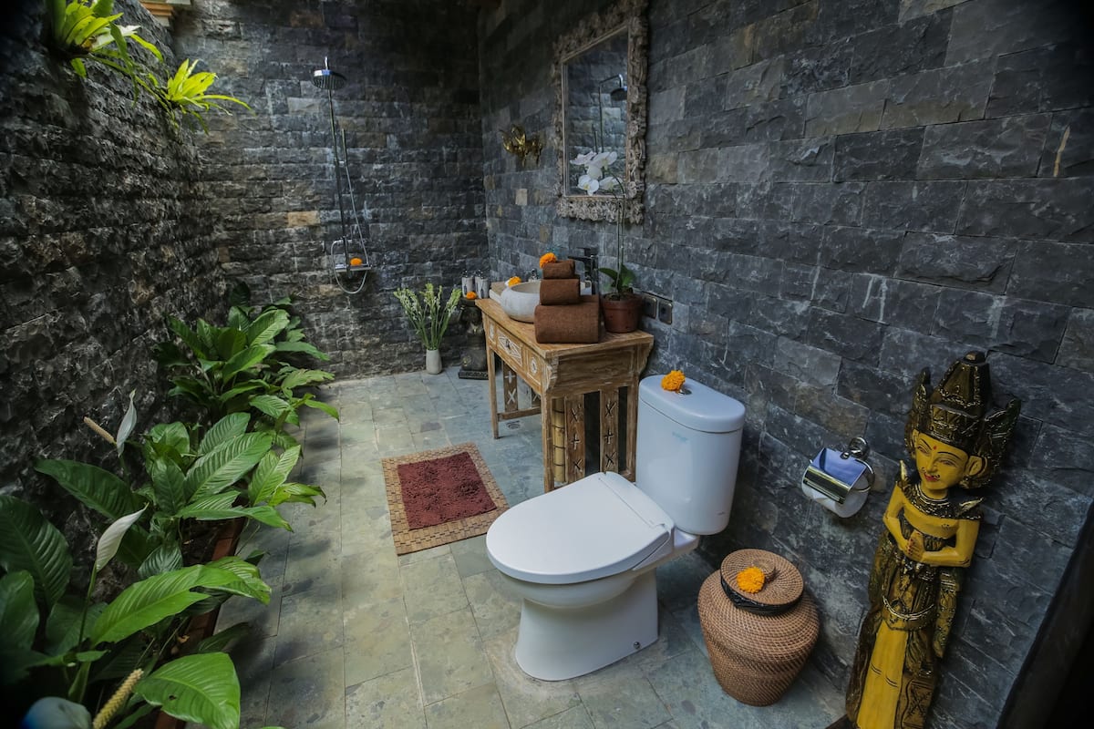 A bathroom with a stone wall, a toilet, a wooden vanity, and a statue.