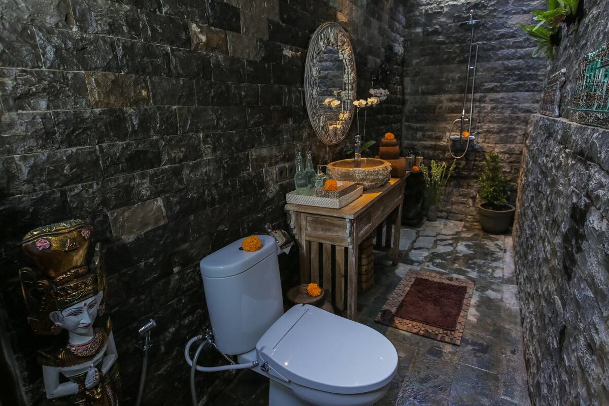 A compact bathroom with a stone wall, a toilet, a sink, and a mirror.