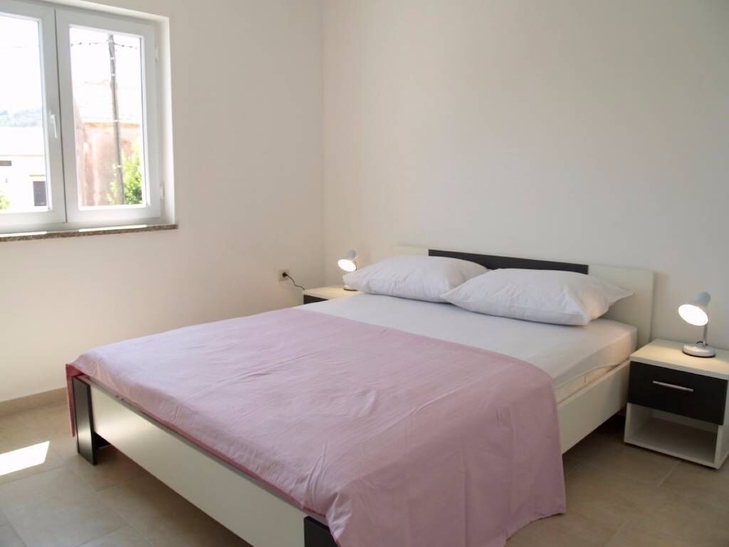 A bedroom with a bed, two bedside tables, a window, and a nightstand with a lamp.