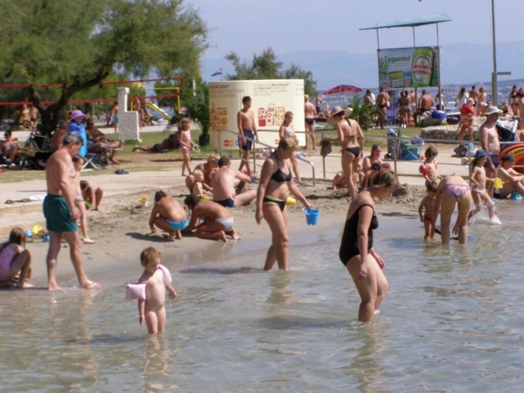 A crowded beach with people in swimwear, a lifeguard tower, and a beach umbrella.