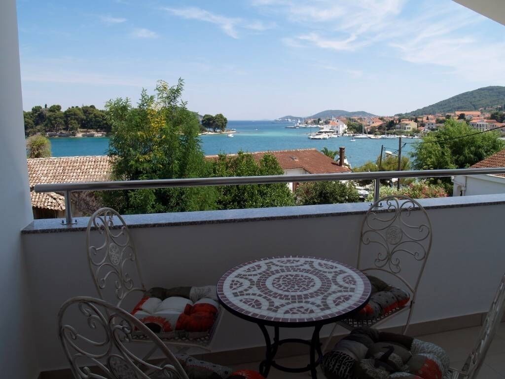 A balcony with a view of a coastal town, a round table, and two chairs.