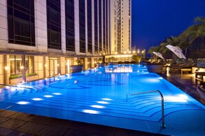 A swimming pool with a blue-lit design, surrounded by lounge chairs and umbrellas, with a high-rise building in the background. - Mingzuo Hotel Zhongshan (Zhongshan)