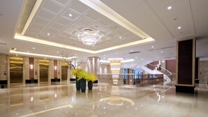 A spacious lobby with a polished marble floor, a grand chandelier, and a staircase leading to upper levels.