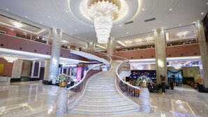 A spacious atrium with a grand staircase, multiple levels, and a central chandelier.