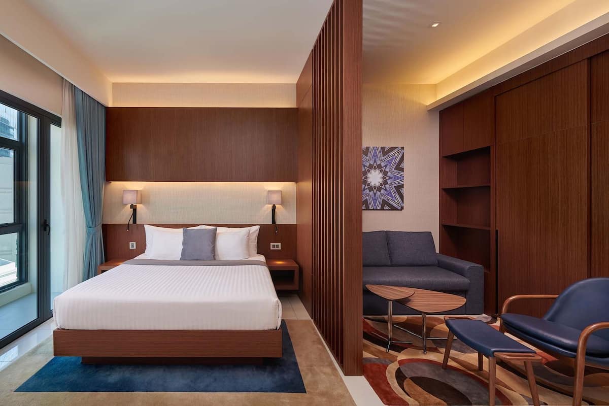 Une chambre d’hôtel moderne avec un grand lit, des lampes de chevet, un canapé, une petite table et une chaise.