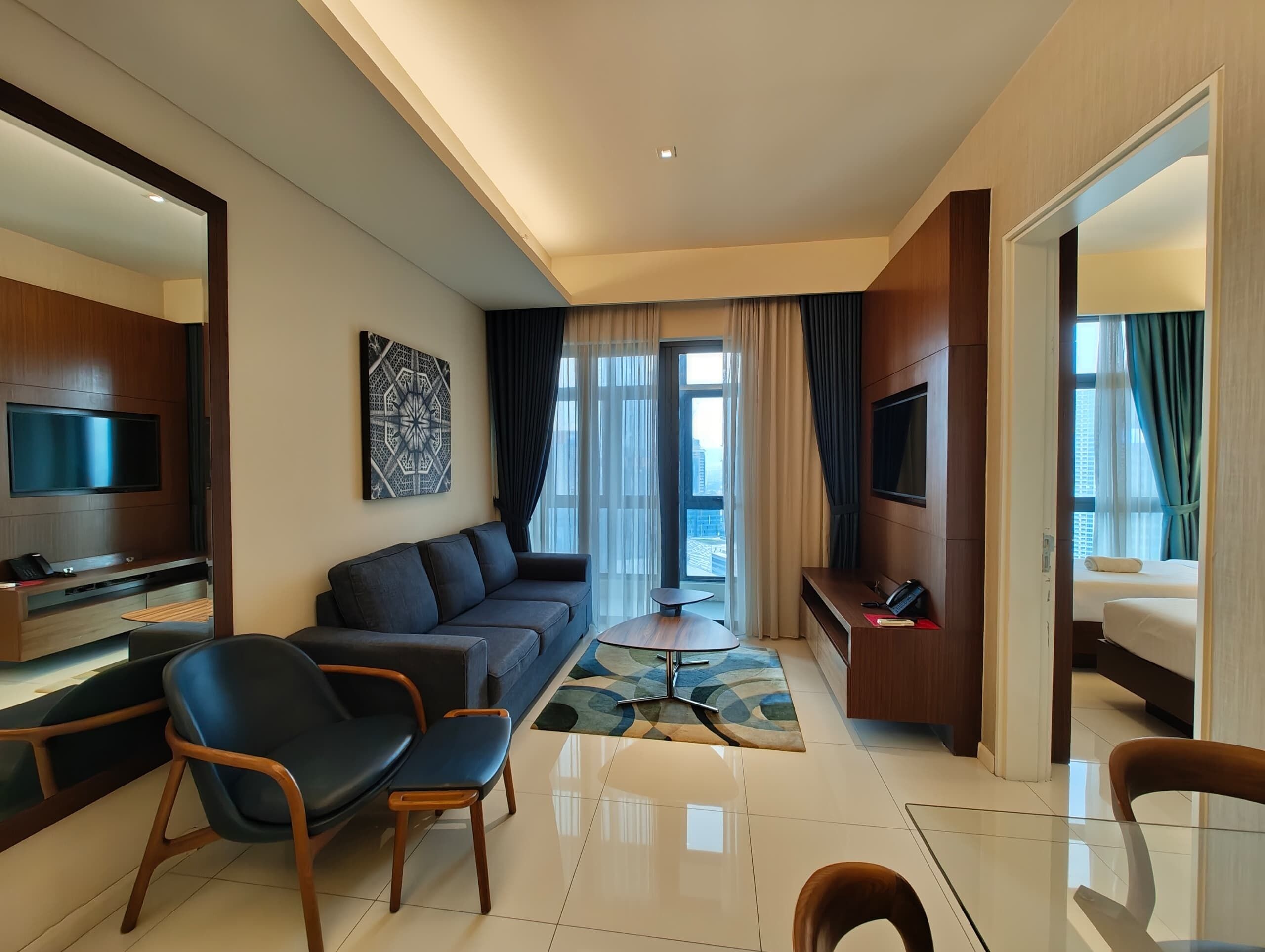 A modern hotel room with a sofa, chairs, a TV, a desk, and a bed.