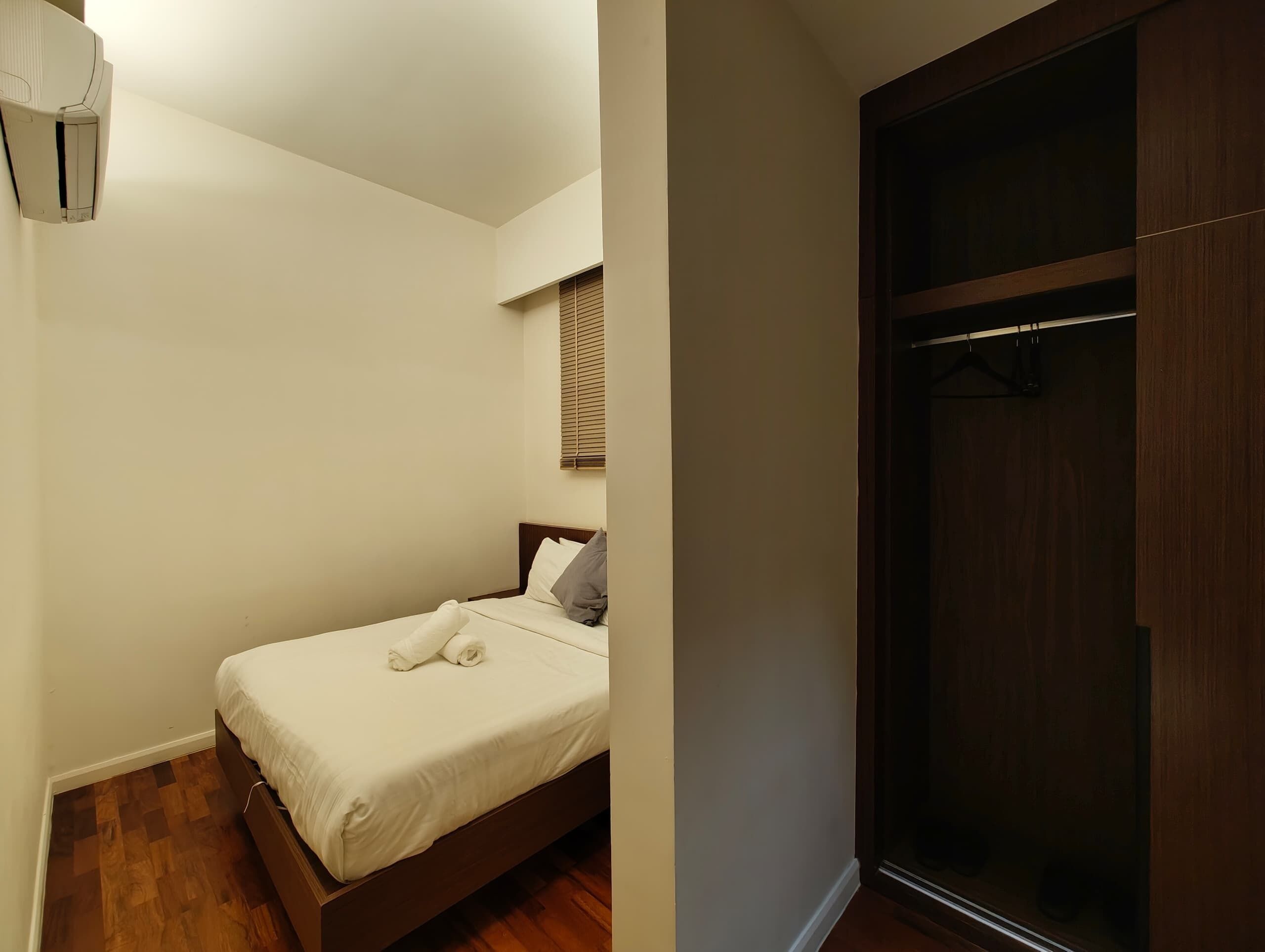 A bedroom with a bed, a wooden floor, a window with blinds, and a wardrobe.