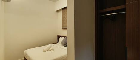 A bedroom with a bed, a wooden floor, a window with blinds, and a wardrobe.