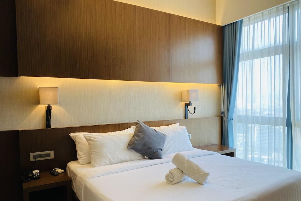 Une chambre d’hôtel avec un grand lit, deux tables de chevet, une lampe fixée au mur et une vue sur la ville par la fenêtre.