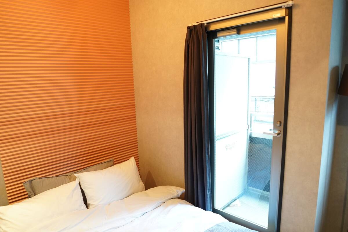 A hotel room with a bed, a ceiling light fixture, a window with curtains, and a door.