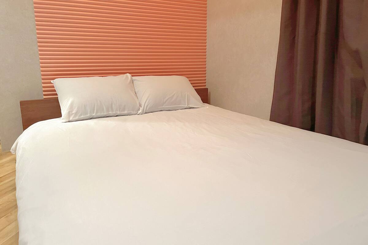 A bed with white bedding and two pillows, a wooden headboard, and a striped orange wall behind it.