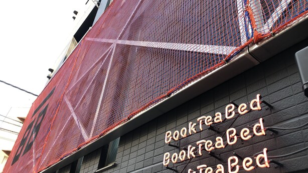 A building with a sign reading "BookTeaBed" and a red netting structure on the side. - Book Tea Bed Shinjuku-Gyoen (Tokyo)