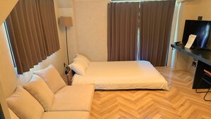 A hotel room with a bed, a sofa, a desk with a computer, and a lamp. - Book Tea Bed Shinjuku-Gyoen (Tokyo)