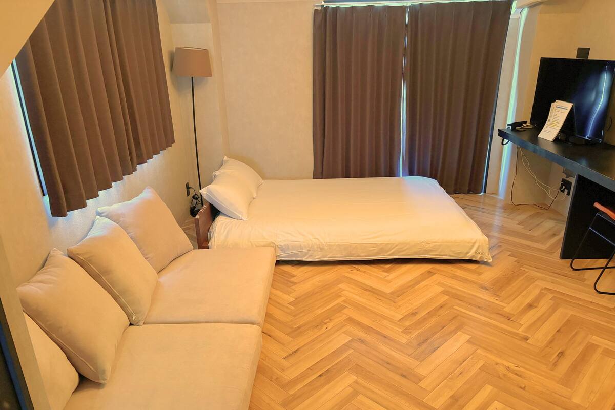 A hotel room with a bed, a sofa, a desk with a computer, and a lamp.