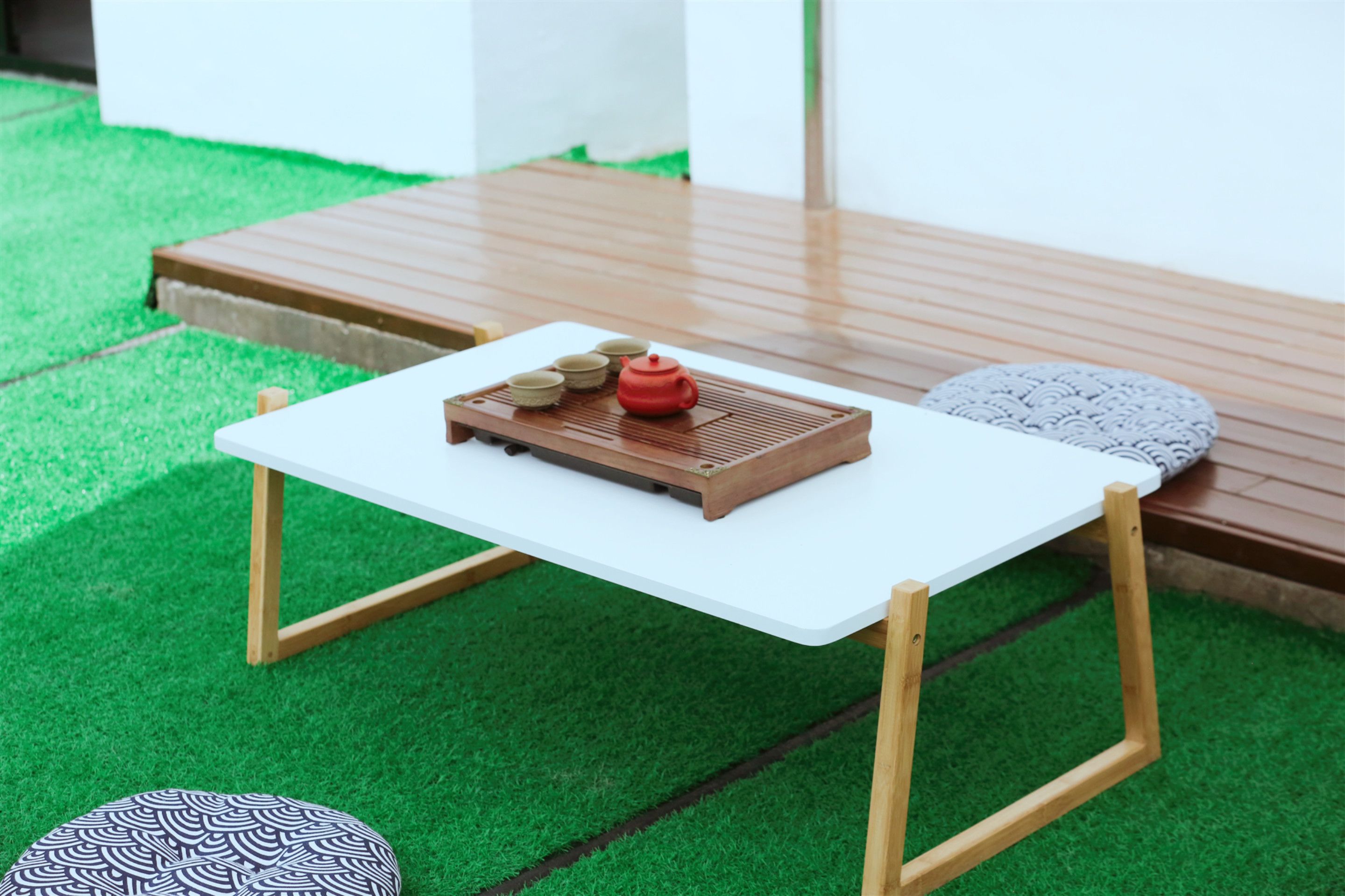 A small white table with a red teapot and tea cups on a green artificial grass floor.