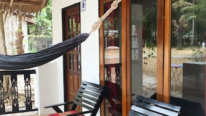 A covered outdoor seating area with a hammock, two wooden chairs with red cushions, and a glass door with a number sign. - Papillon Bungalows (Ko Lanta)