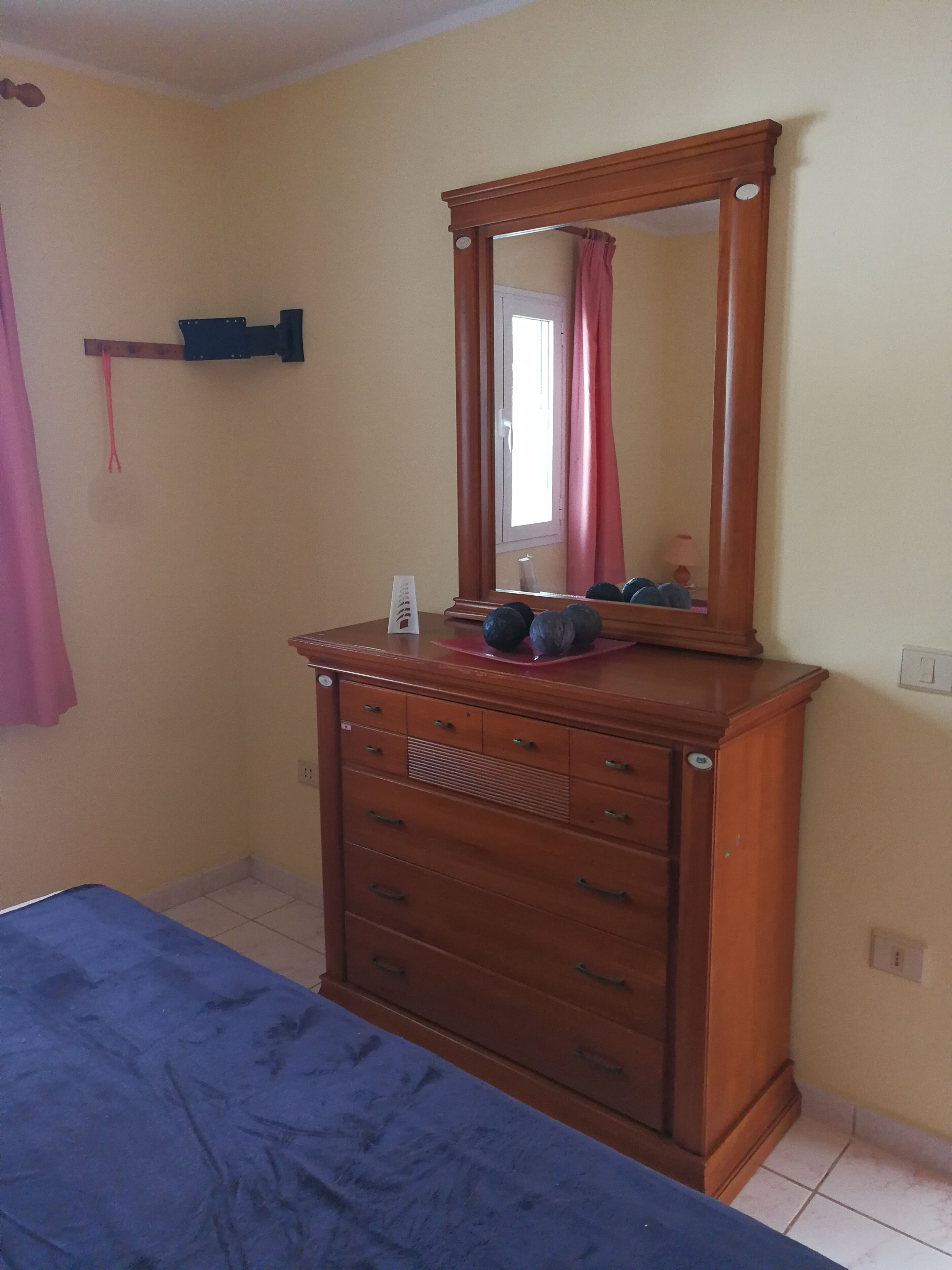 A bedroom with a wooden dresser, a mirror, and a bed.