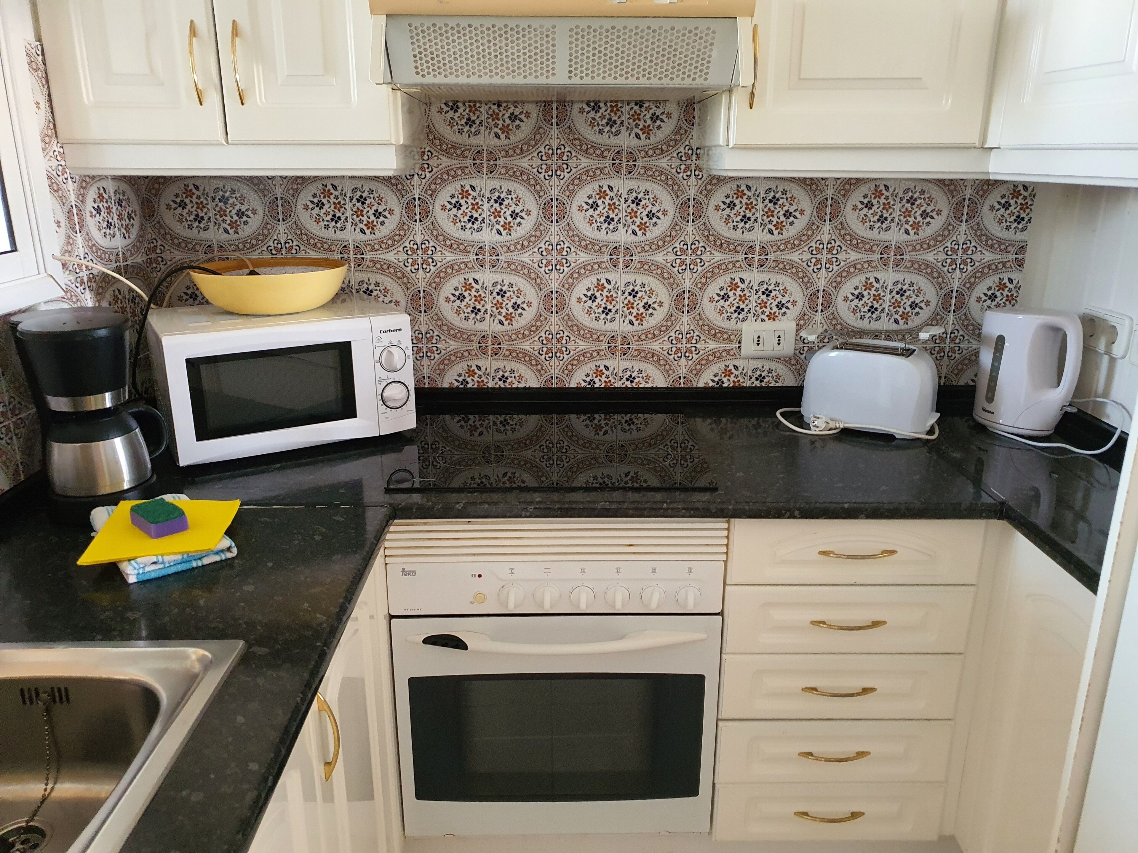 Una cocina compacta con armarios blancos, microondas, tostadora, hervidor y cafetera.