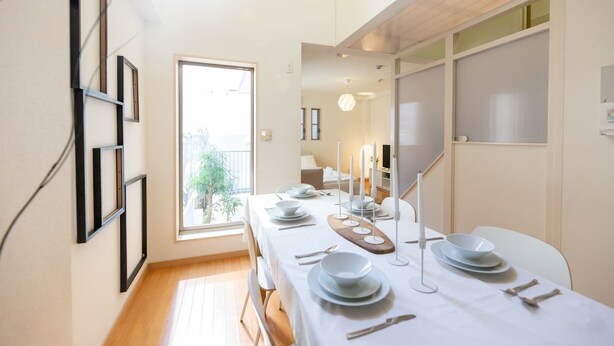 Un coin repas avec une longue table dressée pour quatre personnes, un plancher en bois et une vue sur l’extérieur par une fenêtre.