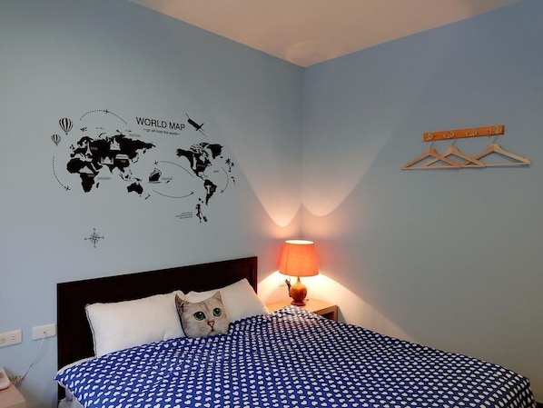 A bedroom with a world map wall art, a bed with a blue polka dot bedspread, a wooden hanger rack, and a bedside lamp. - Yushow Library Villa (Nanzhuang)