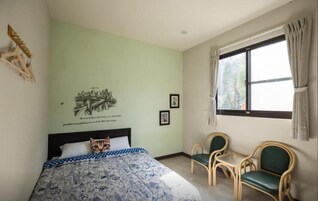 Un dormitorio con cama, dos sillas, un ventanal con cortinas y decoración en la pared.