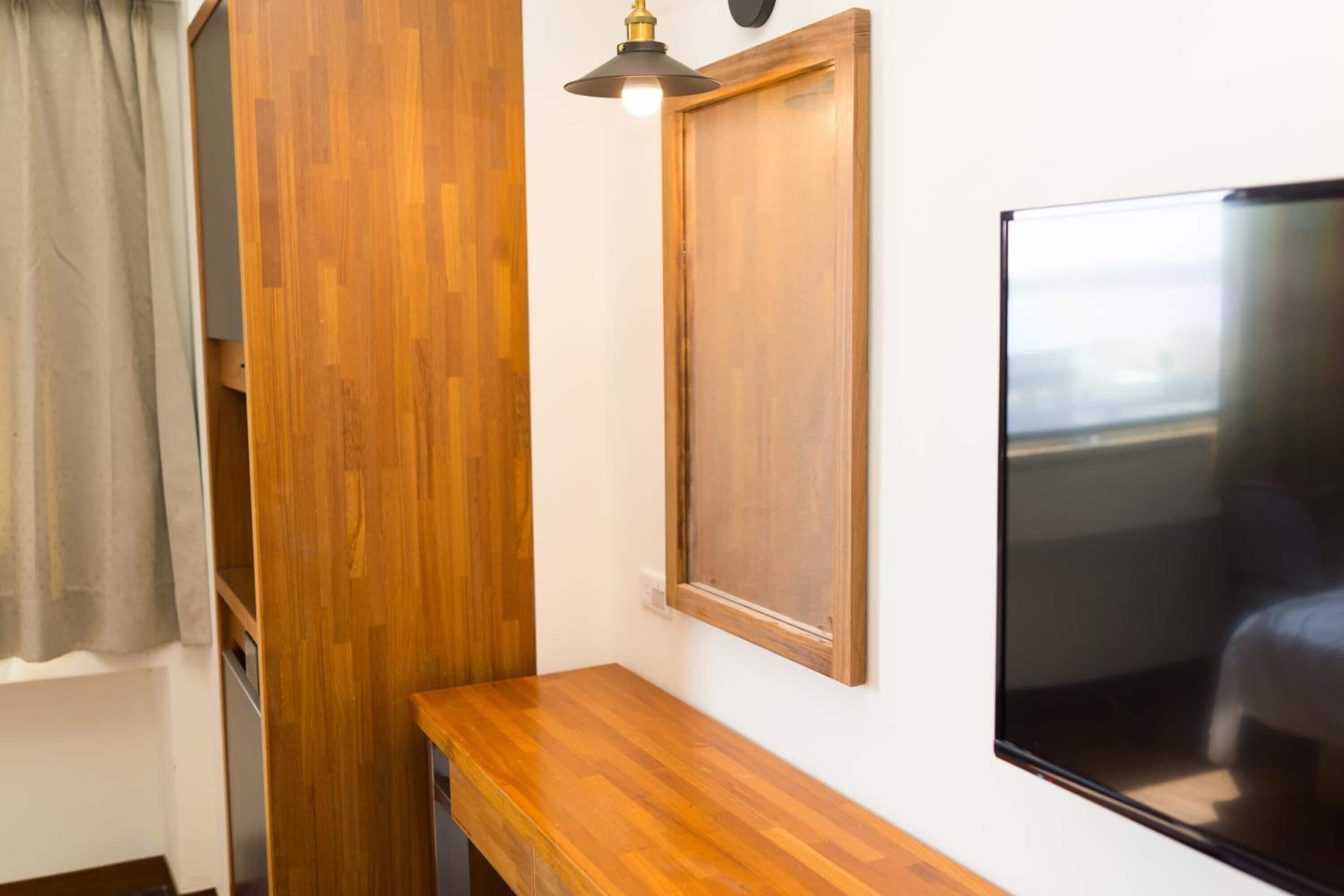 A room with a wooden floor, a wooden bench, a wall-mounted TV, and a ceiling light fixture.