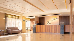 A hotel reception area with a wooden reception desk, a sofa, and a large window with curtains. - Bowa Hotel (Magong)
