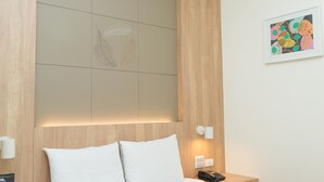 A hotel room with a bed, a nightstand, a wall-mounted light, and a framed artwork. - Bowa Hotel (Magong)
