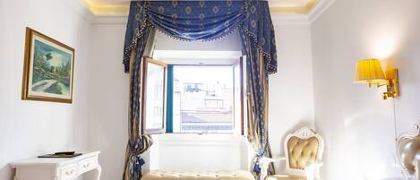 Une chambre d’hôtel avec un lit, un bureau, une chaise, un banc et une fenêtre avec des rideaux.