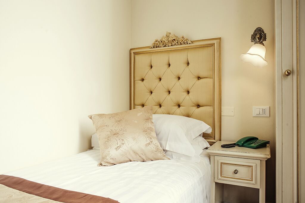 A neatly made bed with a tufted headboard, a bedside table with a telephone, and a wall-mounted light fixture.