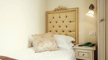 A neatly made bed with a tufted headboard, a bedside table with a telephone, and a wall-mounted light fixture.