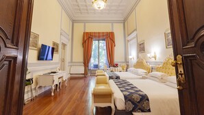 A hotel room with a large bed, a desk, a chair, and a television. - Villa Royal (Florence)
